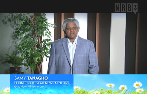 A man in a suit and tie standing next to a plant.